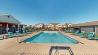 This residential complex in Bargersville, Indiana, boasts an impressive outdoor recreational area centered around a large, inviting swimming pool. The pool area is meticulously designed with a spacious concrete deck, providing ample room for relaxation and socializing. Multiple turquoise lounge chairs are strategically placed around the pool, offering comfortable seating options for residents and their guests.

The complex is characterized by its two-story buildings with tan exterior walls and brown roofing, creating a cohesive and attractive aesthetic. A black metal fence surrounds the pool area, ensuring safety and privacy for residents. Beyond the immediate pool area, well-manicured lawns and pathways contribute to the overall appeal of the property.

The community appears to offer additional amenities, including a clubhouse or common building adjacent to the pool. This structure features a covered porch area, providing shade and a gathering space for residents. The property's layout suggests a focus on outdoor living and community interaction, with open green spaces visible between the residential buildings.

Security seems to be a priority, with gated access to the pool area and possibly to the complex itself. The overall ambiance is one of a well-maintained, family-friendly community with a strong emphasis on outdoor recreation and social amenities. The complex's design effectively balances private residential spaces with shared community areas, creating an inviting living environment.