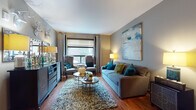 This 2-bedroom, 2-bathroom residence offers a thoughtfully designed single-floor layout that maximizes both comfort and functionality. The living room is a standout space, featuring rich hardwood flooring, large windows that invite natural light, and a warm, contemporary aesthetic accented by bold artwork and layered textures.

The kitchen is equipped with stainless steel appliances, including a refrigerator, range, and built-in microwave, complemented by dark espresso cabinetry, a tile backsplash, and granite countertops. A central island with a pendant light fixture above provides additional prep space and a casual dining option, while recessed lighting illuminates the entire area.

Both bedrooms offer plush carpeting, natural light through well-dressed windows with decorative valances, and a calm, neutral color palette. The primary bedroom features a tufted upholstered headboard and views to the outdoors.

The two bathrooms are finished with dark vanity cabinetry, light countertops, and tile flooring. One bathroom includes a soaking tub and shower combination, while the second offers a clean, efficient layout. Throughout the residence, consistent use of neutral tones, warm wood flooring, and modern fixtures creates a cohesive and inviting ambiance.