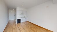 Located at 280 N Oakland Ave in Pasadena, California, this efficiently designed studio unit makes the most of its compact footprint through a clean, modern aesthetic and thoughtful layout. The main living area features warm wood-look flooring and bright white walls that maximize the sense of light and openness. A built-in kitchenette lines one wall, outfitted with white cabinetry, a countertop sink, overhead microwave, and a compact refrigerator — providing all essential cooking and storage functionality in a streamlined package. A wall-mounted mini-split HVAC unit ensures year-round climate comfort. The full bathroom is finished in crisp white, featuring a combination tub and shower with contemporary chrome fixtures and a clean, minimalist surround. Overhead cabinetry adjacent to the bathroom offers additional storage. A sliding glass door leads to a private balcony, where a slatted railing frames open views of the surrounding Pasadena neighborhood, including tree-lined streets and nearby rooftops under the Southern California sky. The balcony also houses the exterior HVAC condenser unit. The overall design is clean, functional, and contemporary, well-suited for those seeking a low-maintenance space in a prime Pasadena location.