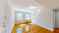 This single-floor residence offers a clean, well-maintained interior defined by gleaming hardwood floors that run throughout the living areas and bedrooms. Multiple rooms benefit from pairs of double-hung windows that invite abundant natural light, casting warm reflections across the polished floors. Several rooms are equipped with ceiling fans, contributing to comfortable air circulation. Radiator units beneath the windows provide supplemental heating, a nod to the building's classic construction.

The living area features crown molding, a ceiling vent, and a six-panel entry door, establishing a tidy, traditional character. Adjacent bedrooms share the same hardwood flooring and window-forward design, with one offering views of mature trees outside. The kitchen is functionally appointed with cream cabinetry featuring decorative raised-panel detailing, dark granite-style countertops, a mosaic tile backsplash, and black appliances including a gas range and dishwasher. Light tile flooring completes the kitchen's practical aesthetic.

The bathroom retains a classic appeal with white subway tile, a black tile accent border, a built-in tub-shower combination, mosaic hex floor tile, and a natural light source from a window above the tub. Overall, the space presents a bright, functional layout with timeless details throughout.