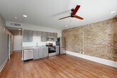 Located in the heart of New Orleans, this single-floor unit at 1717 Religious St blends historic character with modern updates. The open-concept kitchen and living area serves as the centerpiece of the space, highlighted by a striking exposed brick accent wall that lends authentic New Orleans charm. The kitchen is well-appointed with gray shaker cabinetry, granite countertops, stainless steel appliances including a refrigerator, range, microwave, and dishwasher. A ceiling fan overhead and recessed lighting complete the inviting atmosphere of this combined living space, while warm hardwood flooring flows throughout the entire unit. A bright living area adjacent to the kitchen features two windows set within the exposed brick wall, allowing natural light to fill the room. The hallway connects all areas efficiently and includes a stacked washer and dryer unit, adding in-unit laundry convenience. The full bathroom offers a clean, modern finish with a gray vanity, granite countertop, shower-tub combination, and matching hardwood flooring. A dedicated closet provides practical storage. The overall aesthetic balances the historic character of the building with thoughtful contemporary finishes, making this a distinctive and functional New Orleans residence.
