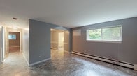 This single-floor unit presents a clean, functional layout finished in a consistent neutral grey palette throughout. The living and dining areas are finished with large-format marble-look tile flooring that extends seamlessly between spaces, providing a cohesive and easy-to-maintain surface. Baseboard heating runs along the walls in multiple rooms, ensuring efficient warmth distribution. Windows overlooking lush greenery allow natural light to filter into the main living spaces, creating a pleasant connection to the outdoors.

The kitchen features rich, warm-toned wood cabinetry with ample upper and lower storage, complemented by laminate countertops and a stainless steel sink positioned beneath a window with garden views. A white electric range completes the setup, while white tile backsplash keeps the space bright and clean.

The bedrooms are finished with plush carpet flooring in neutral tones, offering a comfortable and quiet retreat. Each carpeted room includes baseboard heating and windows that bring in natural light. An additional tiled room with chair-rail detailing provides flexible use as a dining or bonus space. The bathroom features white tile walls surrounding a bathtub and shower combination, marble-look tile flooring, and a clean, minimal finish throughout.