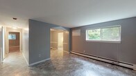 This single-floor unit presents a clean, functional layout finished in a consistent neutral grey palette throughout. The living and dining areas are finished with large-format marble-look tile flooring that extends seamlessly between spaces, providing a cohesive and easy-to-maintain surface. Baseboard heating runs along the walls in multiple rooms, ensuring efficient warmth distribution. Windows overlooking lush greenery allow natural light to filter into the main living spaces, creating a pleasant connection to the outdoors.

The kitchen features rich, warm-toned wood cabinetry with ample upper and lower storage, complemented by laminate countertops and a stainless steel sink positioned beneath a window with garden views. A white electric range completes the setup, while white tile backsplash keeps the space bright and clean.

The bedrooms are finished with plush carpet flooring in neutral tones, offering a comfortable and quiet retreat. Each carpeted room includes baseboard heating and windows that bring in natural light. An additional tiled room with chair-rail detailing provides flexible use as a dining or bonus space. The bathroom features white tile walls surrounding a bathtub and shower combination, marble-look tile flooring, and a clean, minimal finish throughout.