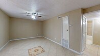 This single-story space presents a practical and cohesive layout highlighted by light beige ceramic tile flooring throughout. The main living area is spacious and open, featuring a ceiling fan with integrated lighting, a textured popcorn ceiling, and neutral-toned walls that create a calm, understated atmosphere. A decorative tile medallion inset into the floor serves as a subtle focal point. Natural light enters through blinded windows, and HVAC vents along with a wall-mounted thermostat indicate climate control throughout.

The bedrooms mirror the living area's design, each equipped with ceiling fans, tile flooring, and windows fitted with horizontal blinds that allow adjustable natural light. The rooms offer clean, uncluttered spaces suitable for a variety of furniture arrangements.

The kitchen is efficiently designed in a galley-style configuration, featuring dark cabinetry, granite-style countertops, a stainless steel sink, a black electric range, and a stone-tile backsplash that adds texture and visual interest to the space.

The bathroom includes a full tub and shower combination with tile surround, a window for ventilation, white upper cabinetry, and a vanity with a granite-style countertop and dark lower cabinet, maintaining a consistent design language with the rest of the space.