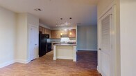 Located at 5550 Bexley Way NW in Concord, NC, this single-floor residence offers a well-designed layout that balances functionality and comfort throughout. The kitchen serves as a central feature of the home, equipped with warm wood cabinetry, granite-style countertops, a full suite of black appliances including a refrigerator, range, microwave, and dishwasher, and a peninsula island with pendant lighting overhead. Track lighting and hardwood flooring complete the kitchen's polished, practical aesthetic. The open layout connects the kitchen seamlessly to the main living area, which continues the hardwood flooring and is bathed in natural light from a large sliding glass door that opens to outdoor views of mature trees, lending the space a bright and airy atmosphere. The bedrooms feature neutral-toned carpet and large windows that invite natural light, creating calm and restful environments. The bathroom is finished with a wood-toned vanity, a tub-shower combination, hardwood flooring, and well-lit mirror above the sink. Throughout the home, clean white trim, neutral wall tones, and consistent finishes contribute to a cohesive and inviting living environment well-suited for everyday living.