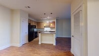 Located at 5550 Bexley Way NW in Concord, NC, this single-floor residence offers a well-designed layout that balances functionality and comfort throughout. The kitchen serves as a central feature of the home, equipped with warm wood cabinetry, granite-style countertops, a full suite of black appliances including a refrigerator, range, microwave, and dishwasher, and a peninsula island with pendant lighting overhead. Track lighting and hardwood flooring complete the kitchen's polished, practical aesthetic. The open layout connects the kitchen seamlessly to the main living area, which continues the hardwood flooring and is bathed in natural light from a large sliding glass door that opens to outdoor views of mature trees, lending the space a bright and airy atmosphere. The bedrooms feature neutral-toned carpet and large windows that invite natural light, creating calm and restful environments. The bathroom is finished with a wood-toned vanity, a tub-shower combination, hardwood flooring, and well-lit mirror above the sink. Throughout the home, clean white trim, neutral wall tones, and consistent finishes contribute to a cohesive and inviting living environment well-suited for everyday living.