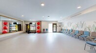 Located at 2545 Jessamine Grove Drive in Indian Land, SC, this well-appointed fitness and activity studio offers a bright, open layout designed to accommodate a variety of group activities and exercise classes. The space is finished with smooth, light-colored flooring throughout, contributing to a clean and airy atmosphere. Recessed lighting across the ceiling provides even, consistent illumination across the entire floor area.

A standout feature is the large floor-to-ceiling mirror wall framed in warm wood trim, which visually expands the space and is ideal for movement-based activities. Adjacent to the mirror, a wall-mounted flat-screen television adds a functional media element for instructional or entertainment use. Built-in cabinetry beneath the TV offers convenient storage.

The studio is equipped with fitness accessories including stacked exercise balls and a rack of resistance bands and free weights, making it ready for a range of fitness programming. Seating lines one wall, accommodating participants during group classes or meetings. A beautifully rendered botanical mural depicting tropical foliage serves as a striking decorative accent along one wall, adding warmth and character to the otherwise minimalist design.

Entry is provided through elegant double doors with wood and glass detailing, as well as a secondary door with exterior access. A climate control system ensures year-round comfort in this functional and welcoming community fitness space.