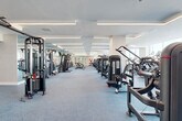 Located at 627 E Dania Beach Blvd in Dania Beach, Florida, this fitness center offers an expansive, single-floor layout designed to accommodate a full range of workout activities. The space is characterized by a clean, modern aesthetic, with a predominantly white color palette, coffered ceilings, and recessed linear LED lighting that creates a bright, energizing atmosphere throughout.

The main workout floor is covered in durable rubber-blend flooring and is organized into distinct training zones. A dedicated strength training area features an extensive selection of selectorized cable machines, multi-station cable systems, free-weight benches, and a full dumbbell rack. Floor-to-ceiling mirrors along multiple walls visually expand the space and support proper form during exercise. Ceiling-mounted monitors provide entertainment throughout.

A separate functional training zone includes kettlebells, stability balls, and open floor space suitable for stretching or group instruction. Structural columns clad in textured, geometric-patterned wallcovering add an architectural detail that softens the industrial feel of the equipment.

Natural light filters in through large windows along one end of the facility, offering outdoor views. The entry area includes a water fountain and glass-panel doors, while additional private rooms provide supplementary fitness or wellness functions.