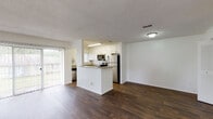 This single-floor residence offers a well-designed open-concept layout that seamlessly connects the living area and kitchen. The living space features rich, dark hardwood-style flooring that extends throughout the common areas, complemented by a sliding glass door that invites natural light and provides outdoor views. A textured ceiling adds a classic touch throughout the main areas.

The kitchen is a functional highlight, featuring crisp white shaker cabinetry, granite countertops, and a full suite of stainless steel appliances including a refrigerator, range, microwave, and dishwasher. A peninsula with a matching granite surface extends into the living area, providing additional prep space and casual seating potential. A window above the double-basin stainless steel sink brings in natural light.

The bedrooms are carpeted for comfort and each features windows that allow for natural light. One bedroom includes a ceiling fan with light fixture. The bathrooms are finished consistently with white cabinetry, granite countertops, and hardwood-style flooring. One bathroom features a full tub-shower combination with white tile surround, while the other offers a vanity with a well-lit mirror. The overall ambiance is clean, bright, and move-in ready.