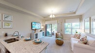 This single-story residence showcases a cohesive coastal aesthetic throughout its thoughtfully designed layout. The open-concept kitchen serves as a central hub, featuring white shaker cabinetry, granite countertops, stainless steel appliances, and a large peninsula with bar seating — ideal for casual dining and entertaining. A tray ceiling adds architectural definition to the kitchen and adjoining living area.

The living room is bright and welcoming, benefiting from abundant natural light through multiple windows and a sliding glass door that opens to a private balcony with outdoor seating. An orb-style chandelier anchors the space visually.

The bedroom offers a tranquil retreat with soft carpeting, a tray ceiling, natural light, and a neutral color palette. A dedicated home office provides a functional, well-lit workspace with carpeted flooring and ample room for furniture.

Two bathrooms are finished with granite vanities and marble-style tile flooring. One features a shower-tub combination, while the other offers a walk-in shower. A dedicated laundry room accommodates a full-sized washer and dryer with additional shelving for storage.

Throughout, neutral tones, soft carpet, and consistent coastal-inspired décor create a calm and cohesive ambiance.