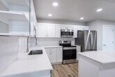 Located at 185 N West Temple in Salt Lake City, Utah, this thoughtfully designed one-bedroom, one-bathroom unit offers a clean, modern aesthetic throughout. Light-toned luxury vinyl plank flooring flows seamlessly across the entire space, complementing the bright, neutral palette of the walls and trim.

The open-concept living and kitchen area serves as the heart of the unit. The well-appointed kitchen features crisp white shaker cabinetry, quartz countertops, a subway tile backsplash, stainless steel appliances including a refrigerator, range, microwave, and dishwasher, and a central island for additional prep and seating space. Recessed lighting illuminates the area throughout.

One of the living areas opens directly to a private balcony through a striking floor-to-ceiling sliding glass door system with sleek black frames, offering panoramic views of the Salt Lake City skyline. Additional windows throughout the unit bring in generous natural light and cityscape views.

The spacious bedroom includes a double-door closet and a large window overlooking the urban surroundings. The full bathroom is elegantly finished with a long double-vanity featuring white cabinetry and quartz counters, an illuminated mirror, and a tiled walk-in shower. Double-door closets and ample storage are present throughout the unit, rounding out this well-designed urban residence.