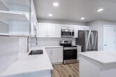 Located at 185 N West Temple in Salt Lake City, Utah, this thoughtfully designed one-bedroom, one-bathroom unit offers a clean, modern aesthetic throughout. Light-toned luxury vinyl plank flooring flows seamlessly across the entire space, complementing the bright, neutral palette of the walls and trim.

The open-concept living and kitchen area serves as the heart of the unit. The well-appointed kitchen features crisp white shaker cabinetry, quartz countertops, a subway tile backsplash, stainless steel appliances including a refrigerator, range, microwave, and dishwasher, and a central island for additional prep and seating space. Recessed lighting illuminates the area throughout.

One of the living areas opens directly to a private balcony through a striking floor-to-ceiling sliding glass door system with sleek black frames, offering panoramic views of the Salt Lake City skyline. Additional windows throughout the unit bring in generous natural light and cityscape views.

The spacious bedroom includes a double-door closet and a large window overlooking the urban surroundings. The full bathroom is elegantly finished with a long double-vanity featuring white cabinetry and quartz counters, an illuminated mirror, and a tiled walk-in shower. Double-door closets and ample storage are present throughout the unit, rounding out this well-designed urban residence.
