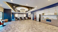 Located at 30 W Broad St in Bethlehem, PA, this single-floor entertainment lounge is a thoughtfully designed communal space combining a private cinema experience with a functional kitchenette and an open lounge area. The space is unified by striking marble-look flooring that flows throughout, complemented by bold navy blue accent walls and gold detailing that lend an air of sophistication.

The screening area is a standout feature, framed by an elegant arched alcove with gold Art Deco-inspired trim lines and a large projection screen. A statement chandelier and patterned tin-style ceiling panels define the overhead design, while sputnik-style wall sconces add a retro-modern ambiance. Plush seating, including curved sofas and accent chairs, creates an intimate theater setting with quality floor-standing speakers for an immersive audio experience.

The kitchenette is well-appointed with wood-tone cabinetry, gold hardware, a textured white stone tile backsplash, open shelving, pendant lighting, a stainless steel French door refrigerator, and a sink — ideal for hosting and entertaining. A charming popcorn machine adds a playful nod to the cinema theme.

The open lounge area benefits from expansive floor-to-ceiling windows and glass sliding doors, filling the space with natural light and providing views of an outdoor terrace. Bistro-style tables and chairs complete this welcoming, versatile gathering space.