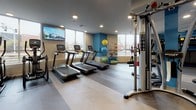 Located at 1935 Stockton Blvd in Sacramento, California, this well-appointed fitness center offers a comprehensive and thoughtfully designed workout facility across a single floor. The space is defined by a striking aesthetic, featuring bold blue abstract wall murals that energize the environment alongside a neutral herringbone-patterned floor that flows throughout.

The facility is organized into distinct training zones. A dedicated cardio area lines the perimeter, equipped with treadmills, stationary bikes, and elliptical machines positioned in front of large floor-to-ceiling windows that invite natural light and offer views of the surrounding neighborhood. Wall-mounted flat-screen televisions provide entertainment during workouts.

The strength training section houses a comprehensive rack of dumbbells and kettlebells, multiple selectorized cable and resistance machines, and a flat weight bench. A separate functional training zone features a fully stocked medicine ball rack, TRX suspension trainers, resistance bands, and stability balls, providing ample space for dynamic movement and bodyweight exercises.

Large glass partitions and interior windows connect the various zones, creating an open and cohesive feel throughout the facility. Recessed lighting and oversized ceiling fans ensure a comfortable environment, while the clean, modern finishes and generous layout make this fitness center a well-equipped destination for a full range of training needs.