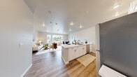 Located at 1779 Village Ln SE in Port Orchard, WA, this thoughtfully designed one-bedroom, one-bathroom unit offers a comfortable and modern living experience across a single floor. The open-concept layout seamlessly connects the kitchen, dining, and living areas, creating an inviting and functional space.

The kitchen is a standout feature, showcasing crisp white shaker cabinetry, striking marble-look quartz countertops with a breakfast bar, matte black fixtures, and stainless steel appliances including a range, microwave, and full-size refrigerator. Recessed lighting adds a clean, contemporary finish.

The living and dining area is bright and airy, bathed in natural light from large picture windows that frame outdoor views. Warm-toned luxury vinyl plank flooring runs throughout, tying the space together with a cohesive, modern aesthetic.

The well-sized bedroom offers a tranquil retreat with windows allowing in generous natural light, neutral walls, and the same warm flooring. The full bathroom features a clean white palette, a tub-shower combo, white vanity cabinetry with matte black hardware, and wood-look flooring. A dedicated utility room completes the layout, adding practical storage and functionality to this efficiently designed home.