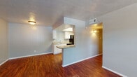 Located at 2811 Custer Pkwy in Richardson, TX, this single-story residence offers a well-designed layout with consistent rich, dark hardwood-style flooring throughout. The open living area is anchored by a pass-through kitchen featuring white cabinetry, granite-style countertops, a breakfast bar peninsula, black appliances including a refrigerator and electric range, and a stainless steel sink — all beneath a bright overhead light panel. The kitchen opens seamlessly to the living space, which is accented by vertical wood paneling on one wall and neutral gray tones throughout, creating a clean and cohesive aesthetic. Bedrooms are generously proportioned, with windows that invite natural light and ceiling fans for added comfort. The primary suite includes a dedicated vanity area with a granite-style countertop and mirror, alongside a spacious walk-in closet with built-in shelving. The bathroom is outfitted with a full-size tub and shower combination with white tile surround. Textured ceilings are present throughout, and the neutral color palette lends a versatile backdrop suitable for a variety of interior styles. The single-floor layout ensures effortless navigation across all living spaces.