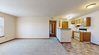 This single-floor, 2-bedroom, 1-bathroom unit offers a functional and straightforward layout designed to maximize its compact footprint. The open-concept living area flows directly into the kitchen, which is separated by a half-wall peninsula counter — ideal for casual dining or additional prep space. The kitchen is well-equipped with oak-toned cabinetry offering ample storage, a white electric range, refrigerator, and a double sink, all set atop durable tile-pattern flooring. Track lighting illuminates the kitchen area, providing a bright and practical workspace.

The living area features neutral-toned carpet and clean white walls, creating a blank canvas that adapts easily to various décor styles. A textured ceiling runs throughout the common areas and bedrooms. Both bedrooms are carpeted and share a similar warm, neutral palette, with each room featuring windows that invite natural light and views of the surrounding exterior. The primary bedroom provides a comfortable and well-proportioned space.

The full bathroom includes a tub-shower combination, a toilet, and a single vanity with an oak cabinet base and mirror, finished with tile flooring consistent with the kitchen. Three hallways connect the rooms efficiently, and a dedicated entrance completes the layout, offering a welcoming transition into the living space.