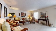 Located at 5743 Kingfish Dr in Lutz, Florida, this single-story home offers a well-organized layout with distinct living spaces designed for comfortable everyday living. The generously sized living room serves as the heart of the home, featuring soft carpeting, a textured ceiling, and ample wall space adorned with framed artwork. Natural light filters in through sheer curtains, creating a bright and welcoming atmosphere. A dedicated seating nook adjacent to the living area provides an intimate retreat, accented by tropical-themed wall art that complements the home's warm Florida character.

The formal dining room is a standout space, highlighted by a large sliding glass door fitted with vertical blinds that frame outdoor views and invite abundant natural light. The room comfortably accommodates a full dining set, making it well-suited for entertaining. A pass-through to the kitchen adds functional connectivity between spaces.

The kitchen features light wood cabinetry, tile flooring, and black appliances including a refrigerator, range, and dishwasher, offering practical storage and workspace. The bathrooms are clean and functional, each featuring a single vanity with a white countertop, a mirror, and tasteful decorative accents. The overall ambiance of the home is warm, cohesive, and move-in ready.