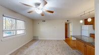 Located at 5577 Dunloe Dr in Virginia Beach, Virginia, this single-floor, one-bedroom, one-bathroom home offers a practical and comfortable layout. The living room is finished with plush carpeting and features a ceiling fan with light fixture, a window allowing natural light, and easy access to the kitchen area. The kitchen is well-appointed with warm wood cabinetry, dark granite-style countertops, white appliances including a refrigerator, electric range with over-the-range microwave, and dishwasher, all set atop light hardwood flooring. Pendant and flush-mount lighting complete the kitchen's functional aesthetic. A secondary kitchen or dining area provides additional counter space and opens into the hallway, which connects the main living areas to the private spaces. The bedroom is carpeted and benefits from a large window with outdoor views of surrounding greenery, offering a bright and peaceful retreat. Two interior doors in the bedroom lead to a dedicated closet, providing ample storage. The bathroom is clean and straightforward, featuring a full tub-shower combination, toilet, and a wood-cabinet storage unit overhead. A utility room rounds out the layout, adding practical functionality to the home.