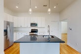 Located at 550 N Holbrook St in Plymouth, Michigan, this well-appointed 2-bedroom, 2-bathroom single-floor residence offers a thoughtfully designed layout with consistent hardwood flooring and crisp white walls throughout. The open-concept kitchen serves as a central highlight, featuring white shaker cabinetry, stainless steel appliances including a refrigerator, range, and microwave, a bold dark quartz-topped island with an undermount sink, and pendant lighting overhead. Recessed lighting and warm hardwood floors complete the kitchen's modern aesthetic. The generously sized primary bedroom is one of the standout spaces, bathed in natural light through a large bay window arrangement and equipped with a ceiling fan. The second bedroom also benefits from multiple windows offering outdoor views of surrounding greenery. Three closets, including a well-organized walk-in with built-in shelving and hanging rods, provide ample storage. The primary bathroom features marble-style tile flooring, a glass-enclosed walk-in shower with matching tile surround, and a dark wood vanity with quartz countertop. The second bathroom offers a tiled tub-shower combination, white vanity cabinetry, and neutral tile flooring. Additional spaces include a laundry room, utility room, and two hallways connecting the layout seamlessly.