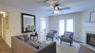 Located at 131 Woodchase Park Dr in Clinton, Mississippi, this single-floor residence offers a thoughtfully designed layout with a welcoming and refined ambiance. The living area serves as the heart of the home, bathed in natural light streaming through a set of classic French doors that open to the outdoors. A ceiling fan with integrated lighting anchors the room, complementing the neutral-toned walls and textured ceiling. The space is generously proportioned, offering ample room for comfortable seating arrangements, as evidenced by the plush sofa and accent chairs that fill the area with warmth and style. A large, bold-framed wall mirror adds depth and visual interest to the room while reflecting light throughout. An adjacent room, visible through an interior doorway, features a fireplace, hinting at additional living or sitting space that continues the home's cohesive, understated aesthetic. The overall atmosphere is clean, airy, and move-in ready, with a neutral color palette that provides a versatile backdrop for a variety of interior design preferences. This residence combines functional living with tasteful design details, making it a comfortable and inviting place to call home.