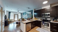 This single-floor residence offers a thoughtfully designed open-concept layout that seamlessly connects the kitchen, dining, and living areas. The kitchen is a standout feature, equipped with dark espresso cabinetry, stainless steel appliances including a refrigerator, range, microwave, and dishwasher, and granite countertops. A peninsula with bar seating and pendant lighting above serves as both a functional workspace and a casual dining spot. Wood-style flooring runs throughout the main living area, adding warmth to the space.

The living room is anchored by a bold teal accent wall adorned with a curated gallery display. A ceiling fan, large windows with blinds, and a glass door provide natural light and outdoor access, creating an inviting, airy atmosphere.

The bedroom continues the teal accent wall theme, complemented by a ceiling fan and a large window that allows generous natural light. It offers a calm, restful environment.

The bathroom features granite countertops, a wide vanity with a large mirror, wood-look tile, and a full soaking tub with tiled surround. A walk-in closet with built-in shelving is accessible directly from the bathroom, adding practical storage to the space.