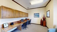 Located in Greer, South Carolina, this single-room business center offers a thoughtfully designed space that balances functionality with a warm, inviting aesthetic. The room is finished with neutral, cream-toned walls, dark wood crown molding, and plush neutral carpeting throughout, creating a professional yet comfortable atmosphere.

A built-in wooden workstation runs along one wall and is equipped with multiple computer terminals and ergonomic task chairs, making it well-suited for productivity. Above the desk, a row of warm-toned wooden upper cabinets provides ample storage while adding a refined, cohesive look to the workspace. Overhead, flush-mounted lighting ensures the area remains well lit.

The opposite side of the room transitions into a lounge area featuring upholstered armchairs and an ottoman, offering a relaxed setting for casual meetings or waiting. A striking arched window with a decorative fanlight allows natural light to filter in and frames views of the lush greenery outside. Elegant double French doors with a transom window serve as the main entry point, enhancing the architectural character of the space. Dark wood door and window trim throughout reinforces the cohesive, polished design. Decorative ceramic vases and a coastal-themed wall painting add subtle artistic touches, completing this well-rounded and highly functional business center.