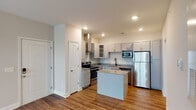 Located at 919 Woody Dr in Graham, NC, this single-story home offers a well-designed layout with modern finishes throughout. The kitchen is a standout feature, equipped with gray shaker-style cabinetry, granite countertops, a full suite of stainless steel appliances including a range, built-in microwave, dishwasher, and refrigerator, as well as a wall-mounted range hood. A central island with a matching granite surface provides additional prep and seating space, while wood-look flooring ties the kitchen and living areas together seamlessly. The open-concept design connects the kitchen to the living area, which transitions to plush carpeting for added comfort. Bedrooms are generously sized with neutral walls, carpet flooring, and ceiling fans with window blinds allowing for natural light control. The primary suite includes access to a walk-in closet outfitted with wire shelving and hanging rods for ample organization. The bathroom features a tub-shower combo with built-in shelving, matte black fixtures, a granite-topped vanity with gray cabinetry, and direct access to the walk-in closet. Recessed lighting throughout the home adds a clean, modern ambiance to every room.