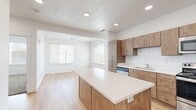 Located at 82 W 500 South St in Provo, Utah, this well-designed one-bedroom, one-bathroom unit offers a thoughtful layout across a single floor. The open-concept kitchen serves as the centerpiece of the living area, boasting warm wood cabinetry, a classic white subway tile backsplash, sleek white quartz countertops, and a generously sized kitchen island ideal for dining or meal prep. Stainless steel appliances — including a refrigerator, range, microwave, and dishwasher — complete the modern kitchen. Light wood-tone flooring flows throughout the main living areas, enhancing the bright, airy feel created by recessed lighting and multiple windows dressed with white blinds. The living area is open and connected to the kitchen, allowing natural light to fill the space. The bedroom features plush wall-to-wall carpeting, clean white walls, and a window that brings in additional natural light, creating a comfortable and restful retreat. The bathroom is well-appointed with a glass-enclosed walk-in shower, wood-tone vanity cabinetry with a white countertop, and direct access to a dedicated walk-in closet with built-in shelving — a practical and organized storage solution. Overall, the unit presents a clean, contemporary aesthetic with a neutral color palette and modern finishes throughout.