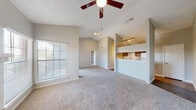 This single-floor residence offers a well-designed open-concept layout highlighted by soaring vaulted ceilings that lend an airy, spacious feel throughout the main living area. The living room serves as the central gathering space, anchored by a classic brick fireplace with a tiled surround and built-in shelving on one side — ideal for display or storage. Plush carpeting, neutral wall tones, and ceiling fans contribute to a comfortable and cohesive atmosphere. Large windows and sliding glass doors flood the space with natural light while providing direct access to the outdoors and neighborhood views. The kitchen features a pass-through design with grey cabinetry, light quartz-style countertops, a white subway tile backsplash, a double stainless steel sink, and a dishwasher, along with a dedicated laundry closet nearby. Track lighting above the kitchen pass-through adds functional illumination. The bedroom is generously sized with carpet flooring, a ceiling fan, a sliding glass door with outdoor access, and direct entry into the bathroom. The bathroom is appointed with grey vanity cabinetry, a tiled tub-shower combination, and wood-look flooring. Throughout the residence, the design maintains a clean, neutral palette with consistent finishes that create a cohesive and move-in-ready environment.
