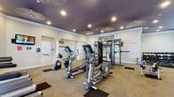 Located at 7521 Windmill Harbor Way in Raleigh, NC, this single-story fitness and recreation facility offers a comprehensive array of amenities designed to support a wide range of athletic and wellness activities.

At the heart of the facility is a full-size indoor basketball court, finished with a polished hardwood floor and marked with regulation court lines. The court soars under a dramatically high ceiling outfitted with recessed lighting, and features boldly painted blue, green, and purple accent bands along the walls, giving the space a vibrant, energetic atmosphere. A regulation backboard and hoop are mounted on one end, while interior windows connect the court to the adjacent fitness areas.

The main fitness room is well-appointed with a diverse selection of cardiovascular and strength-training equipment, including ellipticals, treadmills, a multi-station cable machine, kettlebells, medicine balls, battle ropes, and a punching bag. Deep purple ceilings with recessed lighting and motivational wall signage contribute to an energizing workout environment. Natural light filters in through multiple windows, and a wall-mounted television adds convenience.

A separate spin studio features a polished hardwood floor, a row of stationary cycling bikes, a wall-mounted display screen, and eye-catching blue and green striped wall accents. The studio is bright and airy, supported by recessed fluorescent lighting and ample open floor space for dynamic group fitness sessions.
