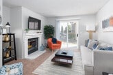 This single-floor residence offers a thoughtfully designed layout that balances comfort and functionality throughout its key living spaces. The living room serves as the heart of the home, anchored by a classic white-tiled fireplace and sliding glass doors that open to a private outdoor area, filling the room with natural light. Soft carpeting and neutral tones create a warm, inviting atmosphere throughout.

The kitchen features a galley-style configuration with dark lower cabinetry contrasted by crisp white upper cabinets, light countertops, and durable wood-look flooring. A black electric range and ample counter space make it a practical and efficient workspace for everyday cooking.

The primary bedroom is a peaceful retreat, carpeted and naturally lit by a large window with vertical blinds, providing both brightness and privacy. A second bedroom offers flexible use as a guest room or home office, also featuring carpet flooring, a window with vertical blinds, and generous floor space.

The bathroom includes a full soaking tub with shower combination, while a louvered door conveniently conceals an in-unit laundry area complete with a washer and water heater, maximizing space efficiency. Throughout the residence, textured ceilings and neutral walls provide a clean, consistent aesthetic that is easy to personalize.