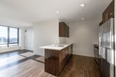 This contemporary single-floor unit offers a thoughtfully designed open-concept layout that seamlessly connects the kitchen and living areas. The kitchen serves as the centerpiece, featuring a large island with a crisp white countertop and an undermount stainless steel sink, complemented by rich dark wood cabinetry, a subway tile backsplash, and a full suite of stainless steel appliances including a French door refrigerator, microwave, dishwasher, and range. Recessed lighting illuminates the space, while expansive floor-to-ceiling windows in the living area flood the unit with natural light and provide open views of the surrounding cityscape.

Rich, dark hardwood flooring runs consistently throughout the main living spaces and bedrooms, adding warmth and cohesion to the modern aesthetic. The bedrooms are generously proportioned, each benefiting from large windows that bring in abundant natural light and urban views, set against clean, neutral-toned walls. The bathroom is finished to a high standard, showcasing a frameless glass walk-in shower with classic white subway tile, a sleek vanity, and modern chrome fixtures. The overall ambiance of the unit is clean, bright, and contemporary, offering a polished urban living environment.