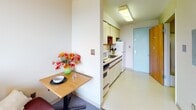 Located at 108 Dryden Rd in Ithaca, New York, this single-floor unit offers a practical and well-organized layout designed for comfortable everyday living. The bedroom is a standout feature of the space, equipped with a large picture window that frames a breathtaking panoramic view of the Ithaca cityscape and the rolling, tree-covered hills beyond. The room includes carpeted flooring, a built-in wood bookshelf unit, and a wall-mounted air conditioning unit, providing both storage and climate comfort. A dedicated study area within the bedroom includes a solid wood desk with built-in drawers and a matching chair, making it well-suited for academic or professional use.

The kitchen is efficiently arranged in a galley-style layout, outfitted with light wood cabinetry, a white refrigerator, an oven with stovetop range, a microwave, and a sink. Adjacent to the kitchen is a compact dining area with a small wooden table, ideal for casual meals. The bathroom features a combined tub and shower with sliding glass doors, a vanity with under-sink storage, and a toilet, all finished with light, neutral tones. Tile-style flooring and a lighted mirror complete the functional bathroom design.