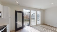 Located at 742 Wayne St in Cincinnati's 45206 neighborhood, this single-floor unit offers a clean, modern aesthetic defined by light-toned luxury vinyl plank flooring, bright white walls, and recessed lighting throughout. The open living area is a standout feature, bathed in abundant natural light streaming through large windows fitted with horizontal blinds and a full-glass black-framed door that opens directly onto a private balcony with metal railings and neighborhood views. The kitchen is thoughtfully designed with crisp white shaker-style cabinetry, open display shelving, solid countertops, a stainless steel sink, and a full suite of stainless steel appliances including an electric range, over-the-range microwave, and dishwasher. A sleek glass-panel interior door connects the kitchen to the adjacent living space, adding a modern architectural touch. The bathroom is finished in a clean, minimalist style featuring a full soaking tub with shower, chrome fixtures, and light wood-look flooring that complements the rest of the unit. The overall ambiance is contemporary and bright, making excellent use of natural light and a cohesive neutral palette throughout.