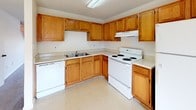 This two-story residence offers a practical and well-organized layout across two floors, providing two bedrooms and two full bathrooms. The kitchen is equipped with warm oak cabinetry, light countertops, and white appliances including an electric range, dishwasher, and refrigerator, all set atop easy-to-clean vinyl flooring. A pantry or storage closet is conveniently accessible from the kitchen area. Both bedrooms are generously sized and feature soft wall-to-wall carpeting and neutral wall tones that create a bright, clean atmosphere. Natural light filters in through large windows, offering views of the surrounding outdoor greenery. One bedroom notably includes dual closets, providing ample storage. Both bathrooms are finished with tile flooring and include a full soaking tub and shower combination, with chrome fixtures and vanity cabinetry. A carpeted staircase connects the two floors, as seen in the architectural overview of the space. Throughout the residence, a consistent neutral color palette, textured ceilings, and clean lines contribute to a simple, functional aesthetic that is easy to personalize.