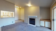 This single-floor residence offers a well-organized and functional layout across several thoughtfully arranged rooms. The living room serves as the heart of the space, featuring plush carpet flooring, neutral-toned walls, and a standout tiled fireplace with a white wood mantle — an inviting focal point for the room. A pass-through window connects the living area to the kitchen, enhancing the open feel between the two spaces.

The galley-style kitchen is efficiently designed with ample cabinetry featuring warm wood accents, tile countertops, and a full suite of white appliances including a coil-top electric range, refrigerator, and dishwasher. Stone-look tile flooring and a window above the sink bring practicality and natural light to this workspace.

The space includes two carpeted bedrooms, each featuring baseboard heating and windows that allow natural light and outdoor views. The neutral tones throughout provide a calm and versatile backdrop.

Two bathrooms serve the residence — one with a single-sink vanity and tile flooring, and another featuring a full tub/shower combination, also finished with stone-look tile. A dedicated laundry area houses a full-size top-loading washer and dryer alongside a water heater, adding significant everyday convenience to the space.