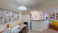 This single-floor residence offers a well-organized layout that balances functionality and comfort throughout its connected living spaces. The kitchen is designed with light wood cabinetry, dark laminate countertops, a double stainless steel sink, and a pass-through opening that looks out toward the entryway, creating a sense of openness. A built-in dishwasher and ample upper and lower cabinet storage add practical utility to the space. Adjacent to the kitchen, the dining area accommodates a four-seat table beneath a dome pendant light, with a decorative metal wall panel providing a contemporary accent. Light tile flooring runs through these areas, contributing to a clean, cohesive aesthetic. The living room features warm hardwood-style flooring, a ceiling fan with integrated lighting, and a wall-mounted shelving unit with a rolling ladder, offering both storage and visual interest. Sliding glass doors open to an outdoor patio with views of surrounding greenery. The bedrooms are carpeted and well-lit by large windows dressed with layered blinds and curtains, lending a calm and restful atmosphere. Two bathrooms complete the unit, each featuring a shower-tub combination and neutral finishes.