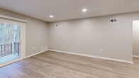 This two-floor unit at Countryside Apartments in Hackettstown, NJ offers a well-designed layout spread across two levels, with the main living areas occupying the upper floor. Light wood-tone luxury vinyl flooring runs throughout the primary living spaces, lending a clean, contemporary aesthetic complemented by neutral gray-toned walls and crisp white trim.

The living room is a generously proportioned space highlighted by recessed lighting and a sliding glass door that opens to a private balcony overlooking a wooded backdrop, bringing in natural light and outdoor views. Adjacent to the living room, the kitchen is efficiently arranged with white shaker cabinetry, granite-style countertops, stainless steel appliances including a gas range, built-in microwave, dishwasher, and refrigerator, plus a built-in desk nook beneath a window.

The spacious primary bedroom features plush wall-to-wall carpeting, a ceiling fan with light fixture, a window with natural light, and direct access to the full bathroom. The bathroom is finished with large-format neutral tile surrounding a soaking tub and overhead rain showerhead. An additional flexible room with a closet and recessed lighting offers versatile use. A staircase connects the entry-level foyer to the main floor above.