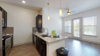 This well-appointed two-story residence offers a thoughtfully designed layout that balances functionality with modern aesthetics. The main living area centers around an open-concept kitchen that seamlessly flows into the living space. The kitchen is outfitted with dark espresso cabinetry, granite countertops, a tile backsplash, and stainless steel appliances including a refrigerator, range, and built-in microwave. A peninsula with an undermount sink serves as both a workspace and casual dining area, illuminated by elegant pendant lighting above. Hardwood-style flooring runs throughout the main level, complemented by a ceiling fan that enhances the bright, airy atmosphere. Natural light pours in through well-placed windows, offering views of the surrounding greenery. A staircase connects the two floors, leading to the upper level where carpeted bedrooms provide comfort and quiet. One bedroom features a large window with an expansive outdoor view. The bathroom is finished with granite countertops, dark cabinetry, a framed mirror, and clean white tile work. The lower level includes an attached garage with an automatic opener, offering generous parking and storage space. Throughout, the space maintains a clean, contemporary palette of neutral tones and quality finishes.