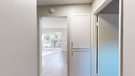 This single-floor unit in Martinez, CA (94553) offers a clean, updated interior with a neutral color palette throughout. The kitchen is well-appointed with white shaker-style cabinetry, quartz countertops, stainless steel appliances including an electric range and refrigerator, and a stainless steel sink — all complemented by light wood-look flooring that extends into the main living areas. The open layout allows natural light to flow between the kitchen and living space, which features a ceiling fan and a wall-mounted heating and cooling unit. Sliding glass doors lead to an outdoor balcony or patio, offering views of surrounding greenery.

The bedrooms are carpeted for comfort and feature textured ceilings, large windows that bring in natural light, and generous closet space with sliding-door closets providing ample storage. The bathroom is outfitted with a tiled shower-tub combination, a window for natural ventilation, wood-look flooring, and a vanity with a light stone countertop. Throughout the unit, clean white trim and soft neutral wall tones create a bright, cohesive atmosphere. The floor plan is functional and efficiently laid out, making excellent use of the available space.