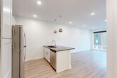 Located on the third floor at 3003 Leavenworth St in Omaha, Nebraska, this efficiently designed unit offers a thoughtful open-concept layout that maximizes every square foot. The combined kitchen and living area serves as the heart of the space, anchored by a sleek central island finished with a dark quartz countertop, an undermount sink, and a modern faucet. Dual polished chrome globe pendant lights hang above the island, adding a contemporary touch. The kitchen features crisp white shaker cabinetry reaching to the ceiling, a subway tile backsplash, and a full suite of stainless steel appliances, including a refrigerator, range, and over-the-range microwave. Light-toned luxury vinyl plank flooring runs throughout, lending warmth and continuity to the open floor plan. The living area benefits from large floor-to-ceiling windows that flood the space with natural light and offer views of the surrounding Omaha neighborhood. A ceiling fan provides additional comfort. The bathroom includes a full tub-shower combination with chrome fixtures and clean white finishes. Recessed lighting throughout keeps the interiors bright and modern, while white walls enhance the sense of openness in this well-appointed urban residence.