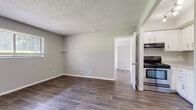 Located at 11413 Grandview Rd in Kansas City, MO, this one-bedroom, one-bathroom unit offers a efficiently designed single-floor layout. Consistent wood-look plank flooring runs throughout the living spaces, complemented by neutral gray walls and white trim that give the interior a clean, cohesive appearance. Textured ceilings add a traditional finish across all rooms.

The living room provides an open feel with a window allowing natural light to filter in, a small wall-mounted shelf, and a floor vent for climate control. It connects seamlessly to the kitchen, which is outfitted with white cabinetry featuring brushed nickel hardware, light speckled countertops, a stainless steel refrigerator, and a stainless electric range with overhead ventilation hood.

The bedroom accommodates essentials comfortably and includes a built-in closet with bifold doors, a shelf, and a hanging rod for organized storage. A window in the bedroom brings in additional natural light. The bathroom features a full-size soaking tub with a shower, surrounded by clean white tile walls. A hallway connects the rooms, contributing to the unit's efficient and straightforward flow throughout.