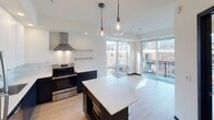 Located at 3011 Holmes Ave S in the Whittier neighborhood of Minneapolis, this contemporary single-floor residence showcases a thoughtfully designed open-concept layout with modern finishes throughout. Light hardwood flooring flows seamlessly across the main living areas, complementing the clean, neutral palette.

The kitchen is a standout feature, outfitted with sleek two-tone cabinetry — crisp white upper cabinets paired with dark lower cabinets — and bright white countertops. Stainless steel appliances include a refrigerator, electric range with a stainless hood vent, and dishwasher. A central island with pendant globe lighting anchors the space, while the open layout connects effortlessly to the living area.

The living space benefits from expansive floor-to-ceiling windows that flood the interior with natural light and provide views of the surrounding neighborhood. A private balcony extends the living space outdoors.

The bathroom features a dark-cabinetry vanity with a white countertop, a large mirror with track lighting overhead, and tiled flooring. A utility area accommodates a stacked washer and dryer, adding everyday convenience. An additional flexible room with hardwood floors offers versatility as a bedroom, office, or storage space. This residence combines modern urban design with practical functionality in a well-connected Minneapolis location.