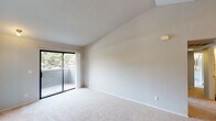 Located at 4005 Cowell Blvd in Davis, CA, this apartment offers a well-designed single-floor layout that balances comfort and functionality. The open living area features plush carpeting, vaulted ceilings, and a ceiling fan, creating an airy and inviting atmosphere. A sliding glass door leads to a private balcony overlooking lush greenery, allowing natural light to fill the space throughout the day. The kitchen is thoughtfully appointed with stainless steel appliances — including a refrigerator, range, and microwave — complemented by white cabinetry, granite-style countertops, a double stainless steel sink, and warm wood-look flooring. Track lighting overhead adds a modern touch. A breakfast bar connects the kitchen to the living area, enhancing the open flow. The bedrooms are carpeted and receive generous natural light through sliding or standard windows with views of the surrounding landscape. The bathroom features wood-look tile flooring, a granite-topped vanity with white cabinetry, and a bathtub with shower. An additional vanity area with a closet provides added convenience. Built-in shelving in the hallway offers practical storage solutions throughout this well-appointed Davis residence.