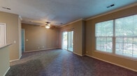 This single-story unit offers a well-organized layout that balances open communal spaces with functional private areas. The living room is generously sized, finished with plush wall-to-wall carpeting and crowned with elegant crown molding. A ceiling fan with a built-in light fixture provides both comfort and illumination, while a sliding glass door leads directly to a private balcony with outdoor views framed by lush greenery. An additional large window floods the space with natural light, enhancing the room's airy feel.

The kitchen is designed for practicality, featuring white cabinetry with ample storage, laminate countertops, and a full suite of white appliances including a refrigerator, electric range, built-in microwave, and dishwasher. A wraparound breakfast bar peninsula separates the kitchen from the living area, creating an open yet defined layout. Tile flooring runs throughout the kitchen, complementing the warm tan wall tones.

The bedroom is a comfortable, carpet-floored retreat with a large window that brings in natural light and outdoor views. The bathroom includes a full tub-shower combination with white tile surround and tile flooring. A dedicated laundry room houses a full-size washer and dryer alongside built-in shelving for additional storage.