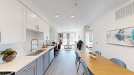 This thoughtfully designed 1-bedroom, 1-bathroom residence offers a clean, modern aesthetic throughout its single-floor layout. The open-concept kitchen, dining, and living area creates a seamless flow that maximizes the efficient use of space. The kitchen is a standout feature, outfitted with stainless steel appliances including a gas range, built-in microwave, and dishwasher, complemented by white shaker cabinetry, gray lower cabinets, quartz countertops, a subway tile backsplash, and a deep stainless steel sink with a commercial-style faucet. The adjacent dining area accommodates a full-sized table and is brightened by crisp white walls. The living room is anchored by light-toned hardwood-style flooring found throughout the unit and features a glass door that opens to an outdoor area, inviting abundant natural light. The bedroom offers a generous window with views of the surrounding greenery, providing a calm and airy retreat. The bathroom includes a full tub-shower combination, gray vanity cabinetry, and a clean white tile surround. Recessed lighting and neutral warm-gray wall tones contribute to a cohesive, contemporary ambiance throughout the entire residence.