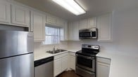 Located in Waco, Texas, this two-story space offers a practical and well-organized layout across two levels. The kitchen is a notable feature, showcasing white raised-panel cabinetry that extends to the ceiling, providing ample storage throughout. A double-basin stainless steel sink is positioned beneath a window fitted with blinds, allowing natural light to filter into the space. Stainless steel appliances, including an electric range with a matching over-the-range microwave, complement the kitchen's clean aesthetic, while a black dishwasher adds a contrasting accent. Light-toned countertops run along the perimeter, offering generous workspace for meal preparation. Overhead fluorescent lighting ensures the kitchen remains well-lit. The white cabinetry and bright surfaces create a crisp, cohesive look throughout the kitchen. The two-story configuration of the overall space suggests a separation of living and private areas across the floors, adding functionality and dimension to the layout. The overall ambiance of the kitchen is clean, utilitarian, and well-maintained, making it a practical space for everyday use.