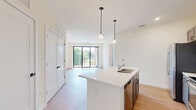 Located at 25 Holland Ave in Albany, NY, this well-appointed 1-bedroom, 1-bathroom unit offers a thoughtfully designed open-concept layout with modern finishes. Light-toned hardwood-style flooring runs throughout the main living areas, complementing the bright, neutral color palette that enhances the sense of space.

The kitchen serves as the centerpiece of the open-concept main area, featuring a large island with a white quartz countertop and a double stainless steel sink. Taupe shaker-style cabinetry pairs with a full suite of stainless steel appliances, including a French door refrigerator, range, and built-in microwave. Elegant pendant lighting hangs above the island, adding a contemporary touch. The living room extends naturally from the kitchen and opens directly onto a private balcony through floor-to-ceiling sliding glass doors, allowing abundant natural light and outdoor views.

The bedroom is carpeted and well-sized, featuring a window with an outdoor view and direct access to a spacious walk-in closet equipped with wire shelving on multiple walls. The bathroom includes wood-toned cabinetry, a light countertop, and grab bar fixtures. A hallway connects the living areas to the private spaces, completing this efficient and modern floor plan.