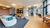 Located at 475 E Broadway in Eugene, Oregon, this expansive amenity floor spans nearly 3,900 square feet of thoughtfully designed communal space. The layout flows seamlessly between distinct activity zones, each with its own character and purpose.

The main lounge anchors the space with generous seating arrangements, plush sofas, and large-format skylights that flood the room with natural light. Floor-to-ceiling glass walls offer sweeping views of the surrounding Eugene cityscape and distant mountain ranges, creating a bright and open atmosphere. Bamboo-style hardwood flooring and a curated selection of original artwork lend warmth throughout.

The game room stands out with its soaring double-height ceilings, a full-size pool table, a wet bar with counter seating, and distinctive teal accent walls featuring geometric tile patterns. Adjacent to this is an impressive indoor bouldering wall, rising dramatically against the same expansive glazed façade, complete with safety mats and panoramic outdoor views.

A dedicated business center offers a built-in desk with multiple computer workstations and task lighting for focused work. Private meeting rooms provide intimate spaces for collaboration, accented by exposed brick walls, bold graphic murals, and sleek carpeted flooring. The welcoming lobby/reception area features warm wood tones, circular decorative wall accents, built-in booth seating, and statement pendant lighting—rounding out a truly comprehensive amenity offering.